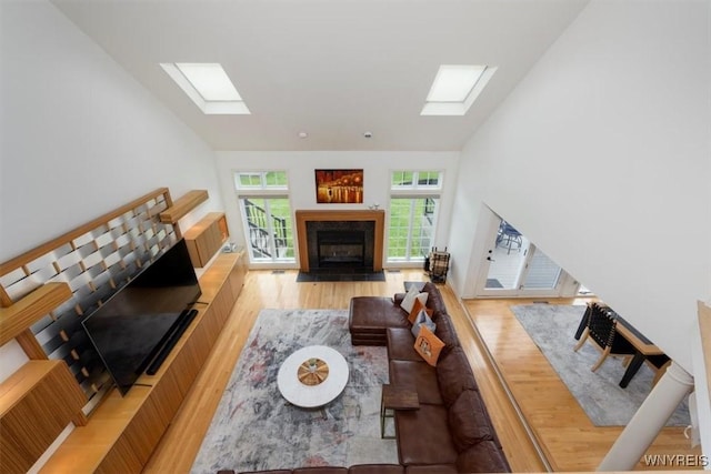 living area featuring a skylight, wood finished floors, lofted ceiling, and a fireplace with flush hearth