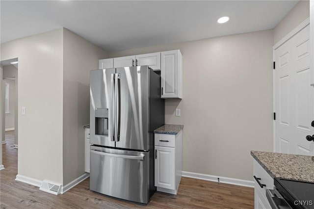 kitchen with stainless steel refrigerator with ice dispenser, baseboards, dark wood finished floors, white cabinetry, and stone counters
