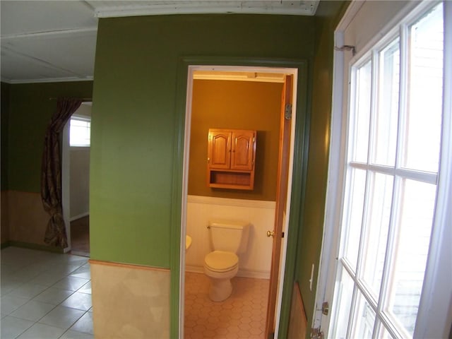 bathroom with tile patterned floors, a wainscoted wall, toilet, baseboards, and crown molding