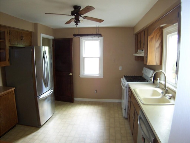 kitchen featuring stainless steel appliances, a sink, ceiling fan, brown cabinetry, and light floors