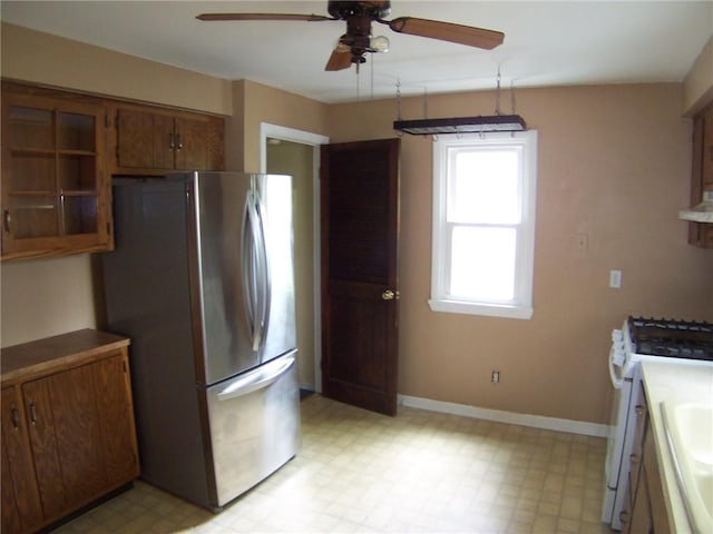 kitchen featuring freestanding refrigerator, white gas stove, ceiling fan, brown cabinets, and light flooring