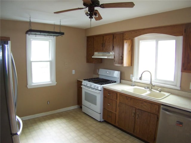 kitchen featuring stainless steel appliances, under cabinet range hood, a sink, light countertops, and brown cabinets