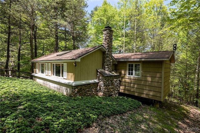 view of side of property featuring a chimney, a shingled roof, and a view of trees