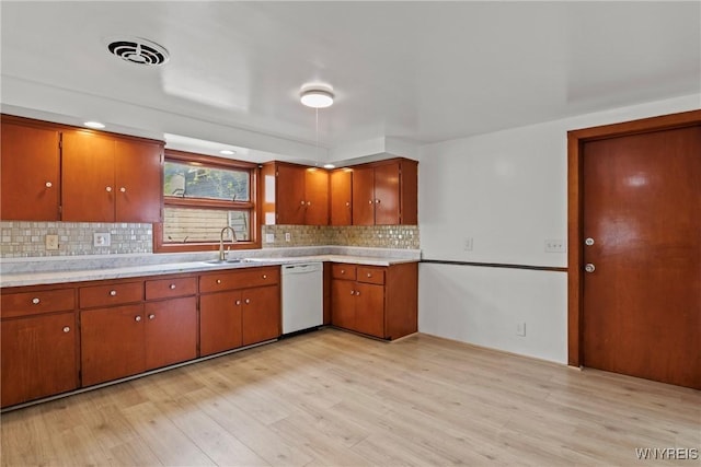 kitchen featuring dishwasher, backsplash, a sink, and light wood finished floors