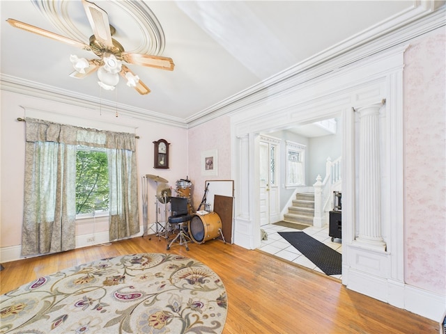 sitting room featuring hardwood / wood-style floors, a ceiling fan, ornate columns, stairs, and ornamental molding