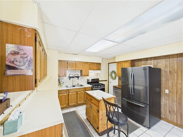 kitchen with appliances with stainless steel finishes, a sink, light tile patterned flooring, light countertops, and wood walls