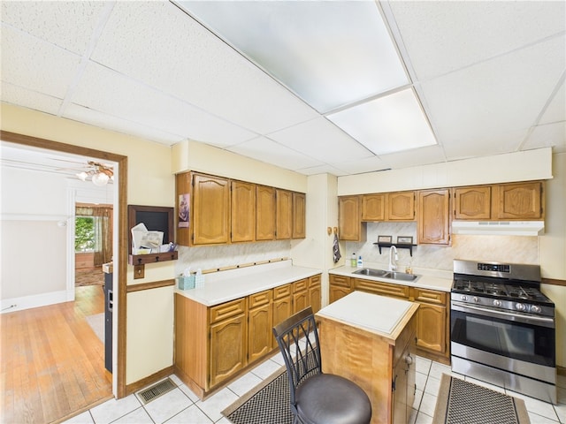 kitchen with stainless steel gas range, under cabinet range hood, a drop ceiling, a sink, and light countertops