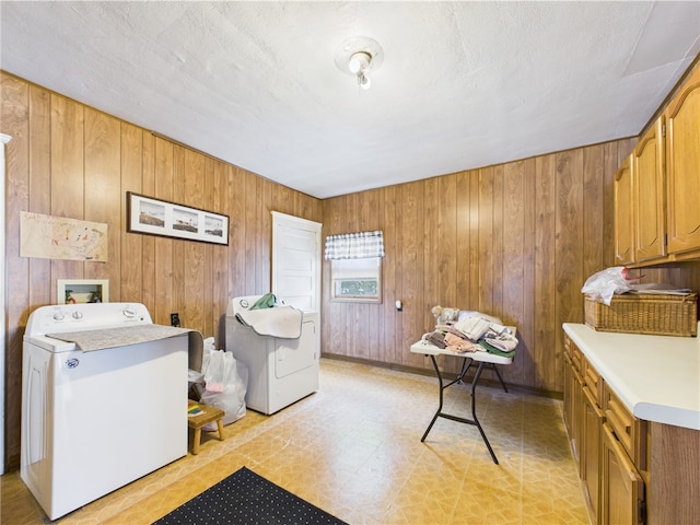 laundry area featuring cabinet space, wood walls, light floors, and washing machine and dryer