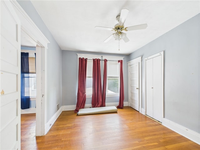 unfurnished bedroom with baseboards, light wood finished floors, two closets, and ceiling fan