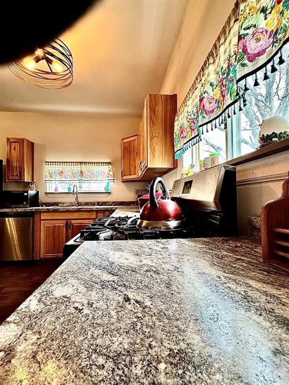 426 Loder St, Barton, NY 14892 - kitchen featuring brown cabinetry, stainless steel dishwasher, range with gas stovetop, stone counters, and a sink
