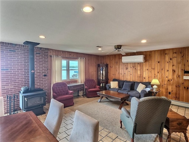 living area with an AC wall unit, a wood stove, a ceiling fan, recessed lighting, and wooden walls