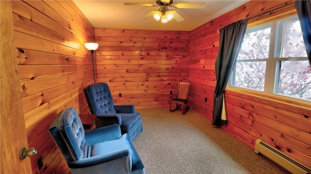 sitting room featuring a baseboard heating unit, wooden walls, carpet floors, and a ceiling fan