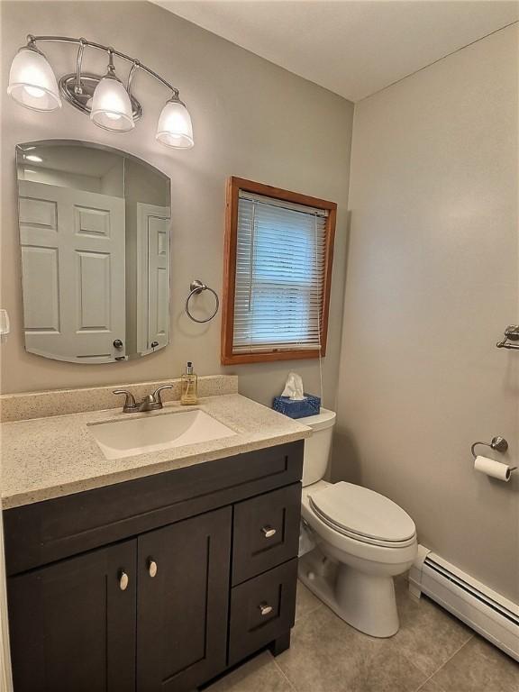 half bath featuring baseboard heating, tile patterned floors, toilet, and vanity
