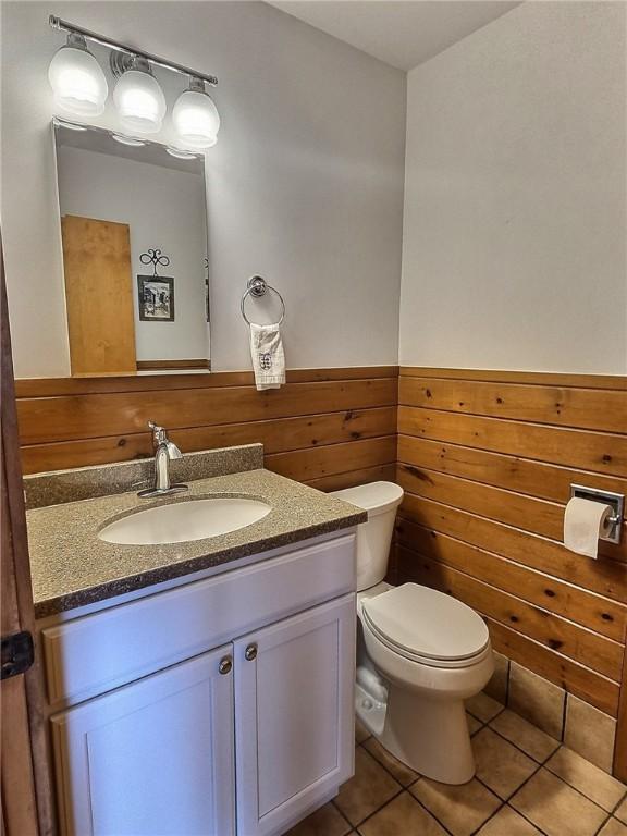 bathroom featuring vanity, toilet, tile patterned flooring, wood walls, and wainscoting