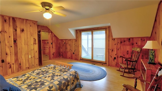 bedroom with wood walls, access to exterior, wood finished floors, and a ceiling fan