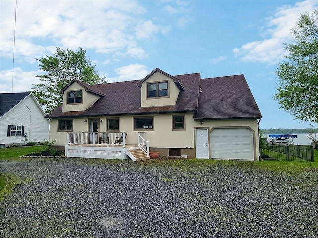 cape cod-style house with an attached garage, fence, gravel driveway, stucco siding, and a shingled roof