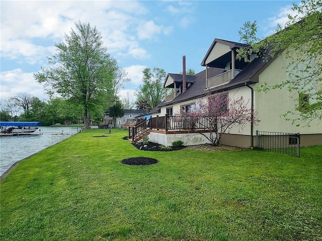 view of green lawn featuring a balcony and a deck with water view