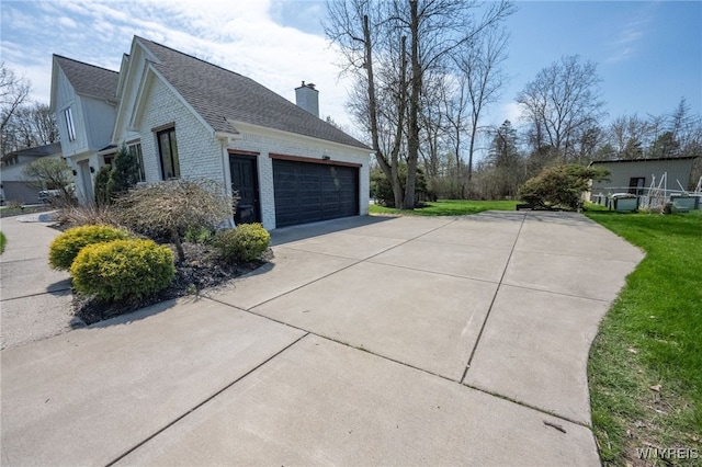 view of side of home featuring a chimney, a shingled roof, driveway, a garage, and brick siding