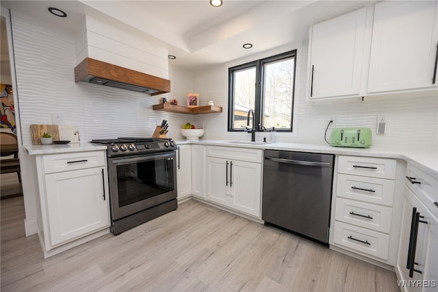 kitchen featuring stainless steel appliances, a sink, backsplash, light wood-type flooring, and white cabinetry