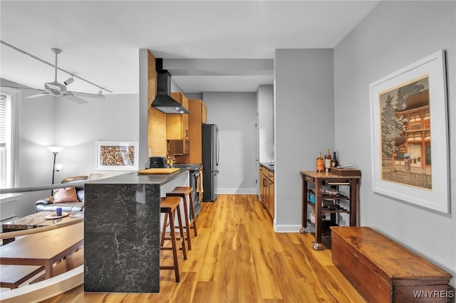 125 Edward St Unit 2G, Buffalo, NY 14201 - kitchen featuring wall chimney exhaust hood, stainless steel appliances, light wood-type flooring, a breakfast bar, and a ceiling fan