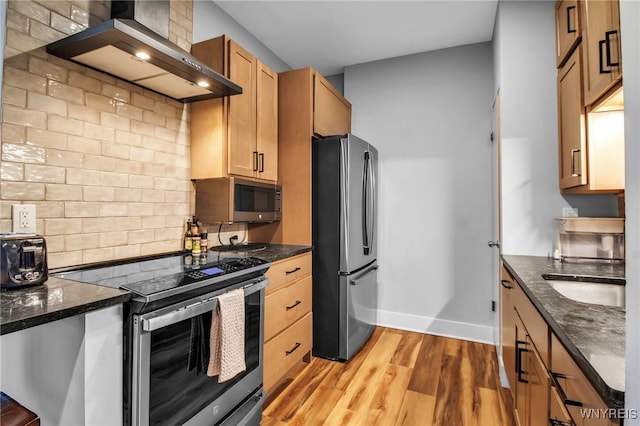 125 Edward St Unit 2G, Buffalo, NY 14201 - kitchen featuring appliances with stainless steel finishes, wall chimney range hood, baseboards, light wood-style flooring, and tasteful backsplash
