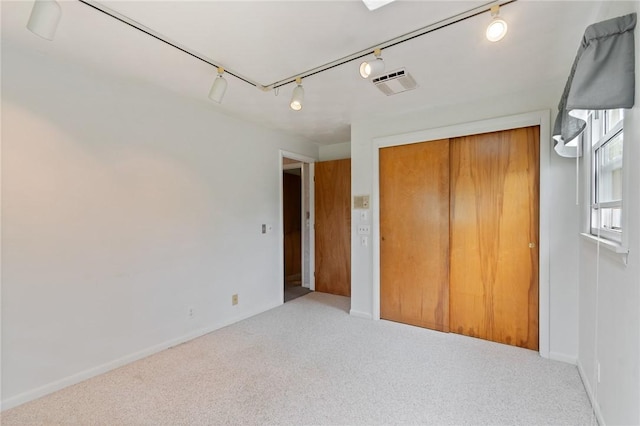 unfurnished bedroom featuring track lighting, carpet flooring, a closet, and baseboards