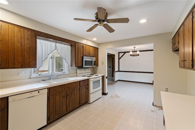 kitchen featuring white appliances, a sink, light countertops, a ceiling fan, and a chandelier