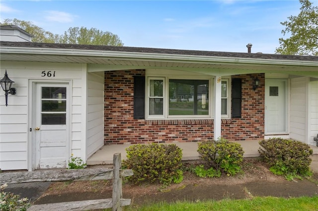 view of exterior entry with brick siding and covered porch