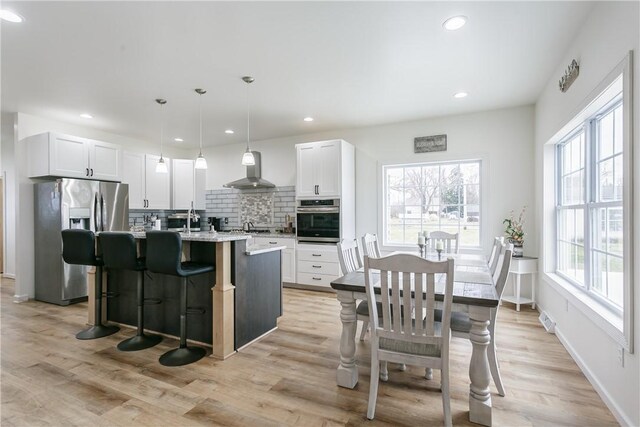 1965 Main St, Carlton, NY 14571 - kitchen with stainless steel appliances, wall chimney exhaust hood, backsplash, a kitchen island with sink, and a breakfast bar area