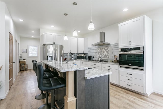 1965 Main St, Carlton, NY 14571 - kitchen with appliances with stainless steel finishes, wall chimney exhaust hood, light stone counters, tasteful backsplash, and a kitchen island with sink