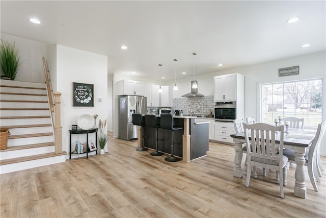 1965 Main St, Carlton, NY 14571 - kitchen featuring appliances with stainless steel finishes, ventilation hood, a kitchen breakfast bar, light wood finished floors, and an island with sink