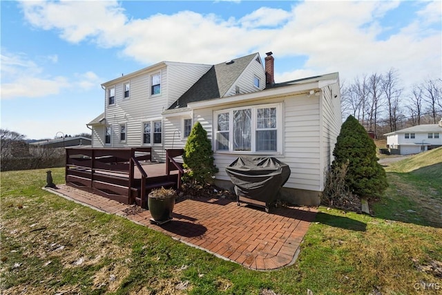 back of property featuring a chimney, a wooden deck, a lawn, and a patio