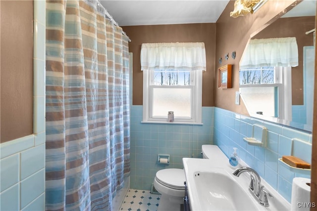 bathroom with tile walls, a sink, toilet, a wainscoted wall, and a shower with curtain