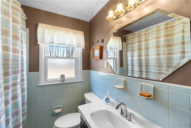 full bathroom with a sink, tile walls, toilet, a wainscoted wall, and a chandelier