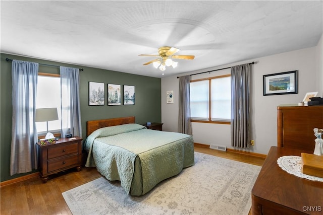 bedroom with multiple windows, wood finished floors, and baseboards