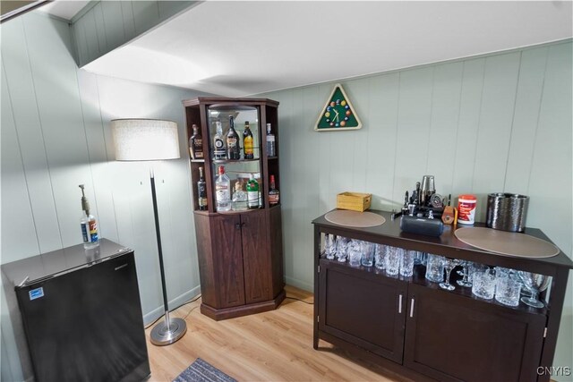 bar with light wood finished floors and refrigerator