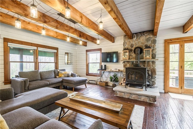 living room with wood-type flooring, healthy amount of natural light, wood walls, beamed ceiling, and a wood stove