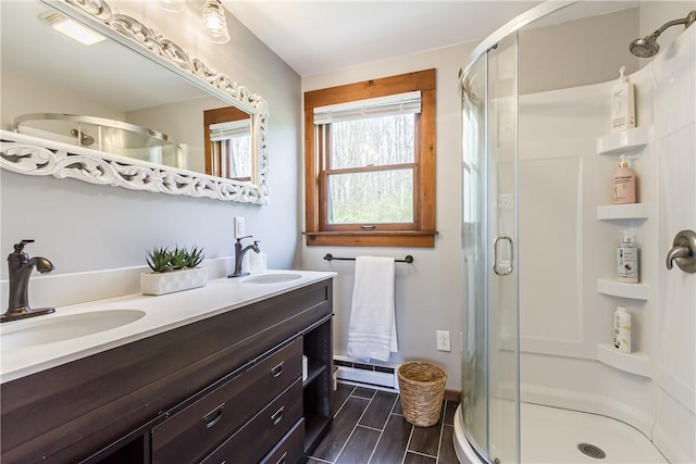 full bath featuring a stall shower, double vanity, baseboard heating, and wood tiled floors