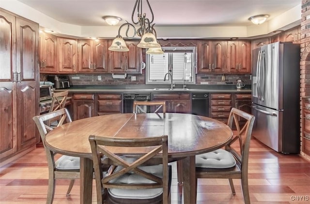 kitchen with stainless steel refrigerator with ice dispenser, a sink, black dishwasher, dark countertops, and light wood finished floors