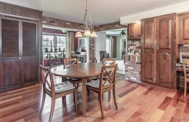 dining area with brick wall, light wood-style floors, and ceiling fan