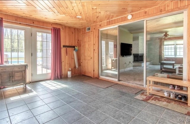 tiled empty room featuring wood ceiling, a ceiling fan, and wooden walls