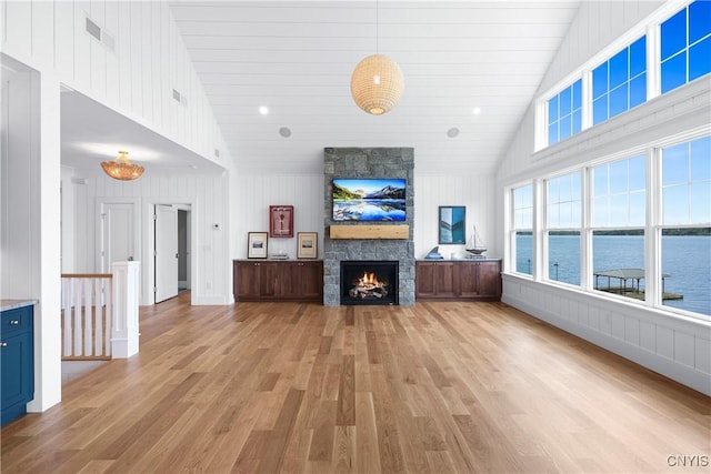unfurnished living room with light wood-style floors, a stone fireplace, high vaulted ceiling, and wooden walls