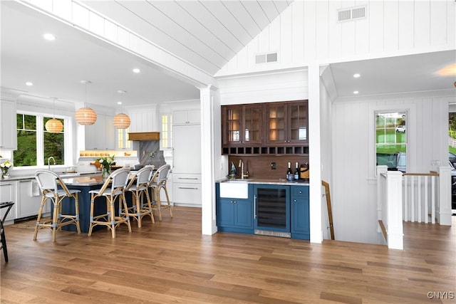 indoor wet bar with beverage cooler, lofted ceiling, light wood-style flooring, dishwasher, and backsplash