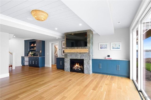unfurnished living room featuring light wood-type flooring, a stone fireplace, a sink, baseboards, and recessed lighting