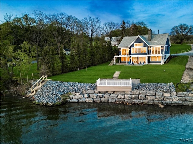 back of house featuring stairs, a chimney, a yard, a water view, and a balcony