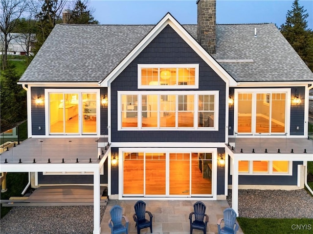 rear view of house with a chimney, a shingled roof, and a patio