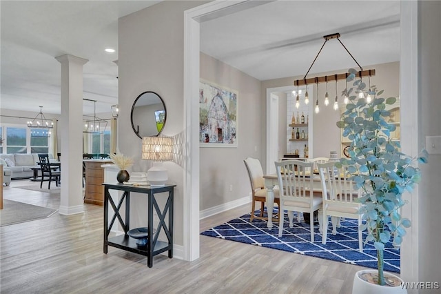 dining space featuring a chandelier, wood finished floors, baseboards, and ornate columns