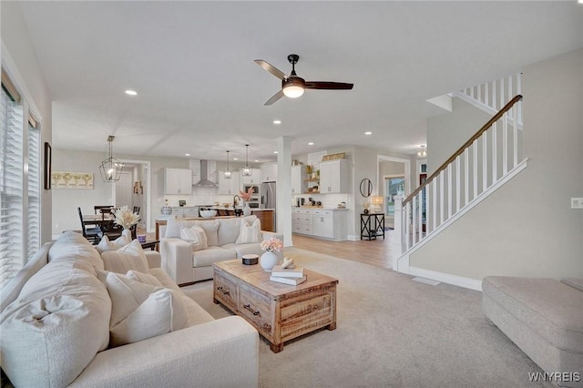 living area featuring stairs, a ceiling fan, light carpet, recessed lighting, and baseboards