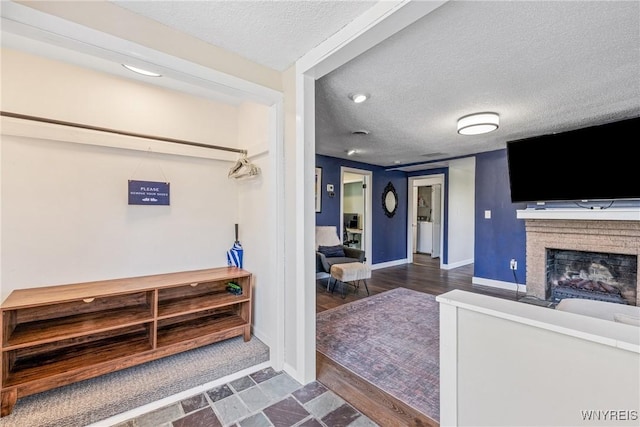 living area with a textured ceiling, baseboards, a brick fireplace, and wood finished floors