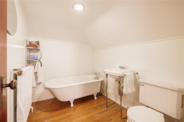 full bath with toilet, radiator, a freestanding bath, vaulted ceiling, and wood finished floors